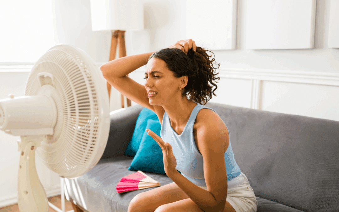 Vrouw zit uitgeput voor een ventilator in haar flat tijdens een zomerse hittegolf - symbolisch beeld voor de stijgende temperaturen in de zomer 2025