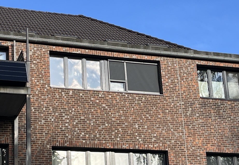 Bakstenen gevel met CLIP'N'SHADE zonwering op twee ramen aan de buitenkant.